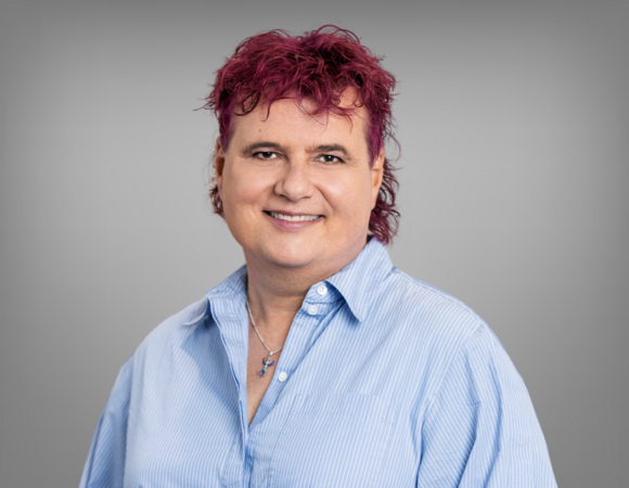 Ein Portrait von Lena Öllinger. Sie hat kurzes rotes Haar und trägt ein blaues Hemd.