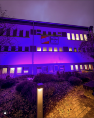 Gebäude bei Nacht in violettem Licht, an der Fassade die Schilder „BAYER“ und „TSV Bayer 04 Leverkusen“.