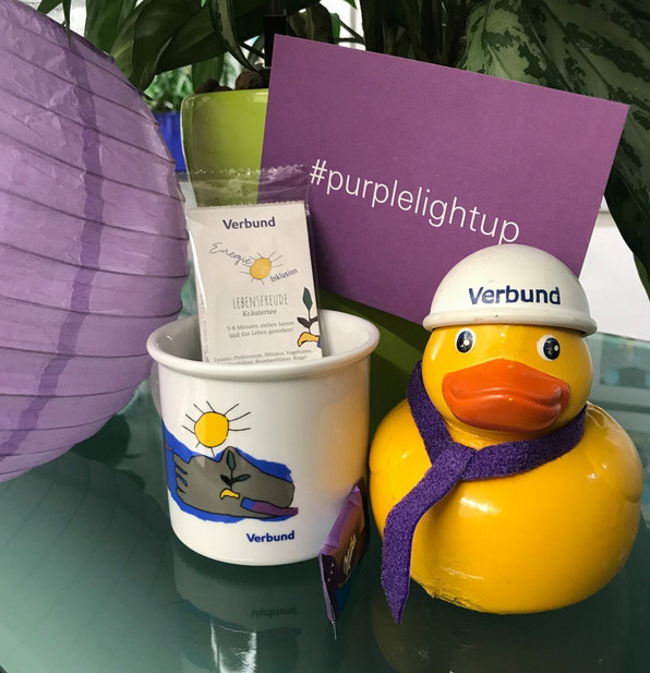 Lila Mitarbeiter:innen Goodies - Tasse, Postkarte und Ente mit lila Schal und Verbund-Helm