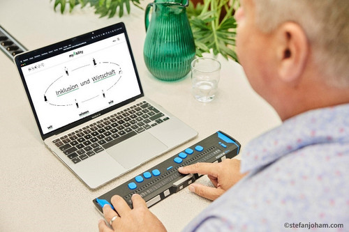 Eine Person sitzt vor dem Laptop und bedient diesen mit Braille-Zeile. Auf dem Bildschirm ist die Webseite www.myability.org geöffnet. Dort steht geschrieben: Inklusion und Wirtschaft.
