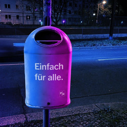 Ein lila beleuchteter öffentlicher Mülleimer an einer Laternenstange mit der Aufschrift "Einfach für alle"