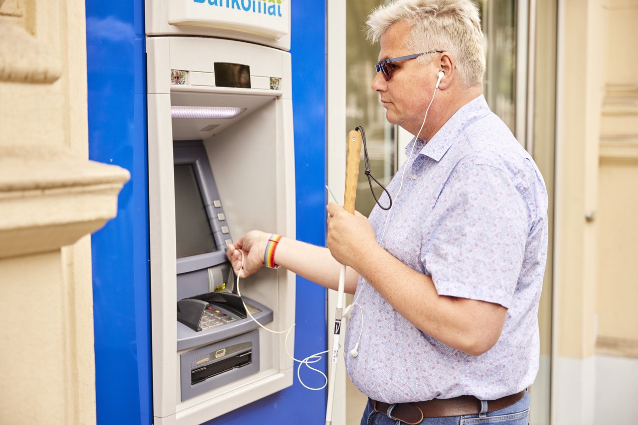 Photo of a male read person with visual impairment at the ATM