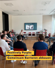 Gruppe an Personen sitzt in einem Sesselkreis. Vorne eine Person die eine Folie von myAbility präsentiert. Text: Positively Purple. Gemeinsam Barrieren abbauen.