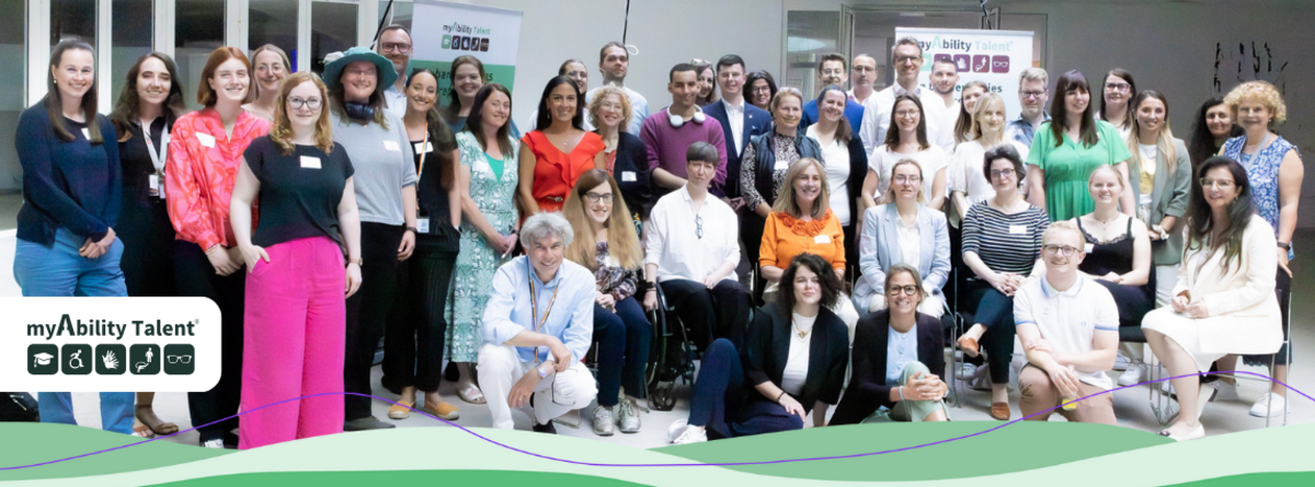 Gruppenbild aus dem myAbility Talent Programm. Ca 50 Personen mit und ohne (sichtbare) Behinderungen lächeln in die Kamera. Die Stimmung scheint locker und fröhlich. myAbility Talent Logo.
