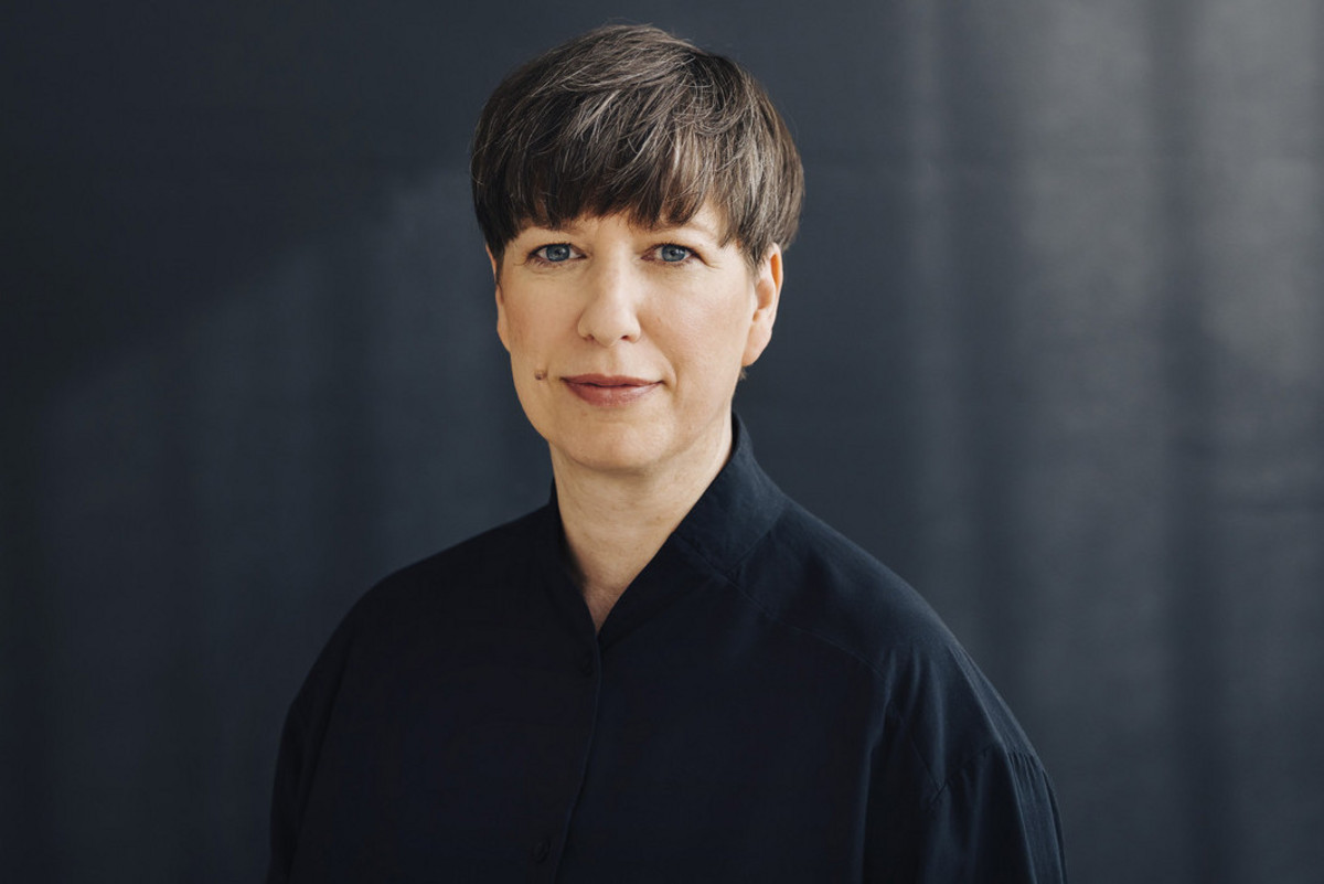 Porträt von Nora Biz mit schwarzer Bluse, dunkelbraunen kurzen Haaren.