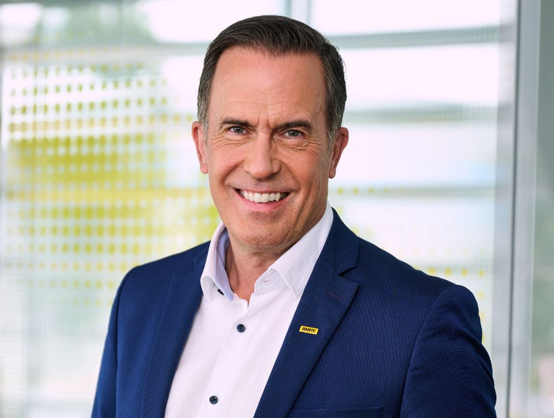 Porträt von Oliver Krupitza. Er hat kurze Haare dunkle Haare. Er hat dunkle Augen und glatt rasiert. Er trägt ein weißes Hemd mit einem dunkelblauem Sakko.