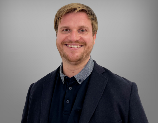 Portrait von Michael Diesner, männlich gelesene Person mit kurzen blonden Haaren und Bart im dunkelbauen Poloshirt und Blazer