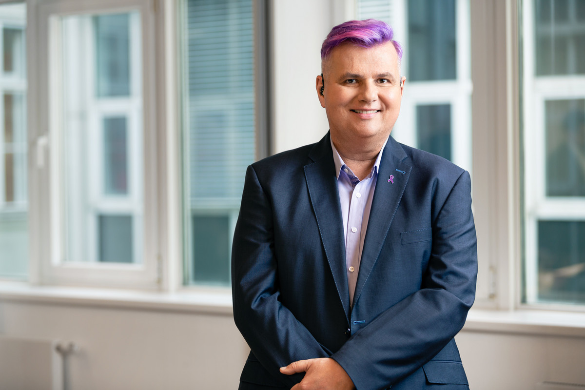 Lena Öllinger_Pressefoto 1 Lena Öllinger hat kurze lila Haare, trägt ein blaues Sakko und lächelt.