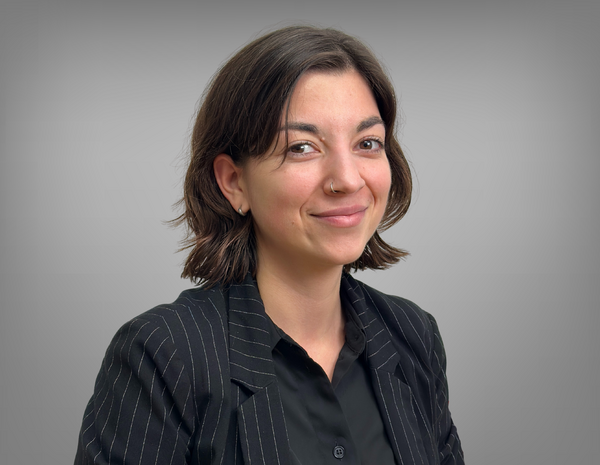 Portrait von Julia Kreuzer. Sie hat schulterlange braune Haare und ein Nasenpiercing. Sie trägt ein schwarzes Hemd mit einem schwarzen Blazer.