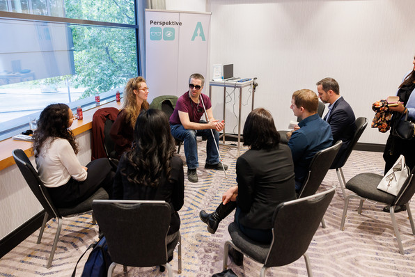 Gruppe von Menschen im Kreis zusammensitzend in einer Workshop-Situation am DisAbility Confidence Day 2022.