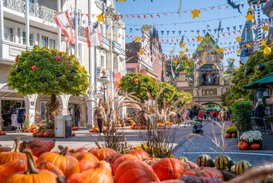 Herbstlich geschmückte Parkstraße mit Kürbissen und Girlanden. Besucher:innen im Hintergrund.
