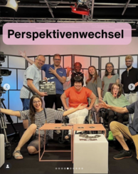 Gruppenfoto im Studio, Text „Perspektivenwechsel“, mehrere Personen, zwei Rollstuhlnutzer:innen, eine Person hält eine Filmklappe.