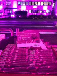 Im Hintergrund ist ein Gebäude lila beleuchtet. Im Vordergrund sind viele Karten, auf diesen steht: "03. Dezember. Internationaler Tag der Menschen mit Behinderungen. #PositivelyPurple. Michelin Logo.""