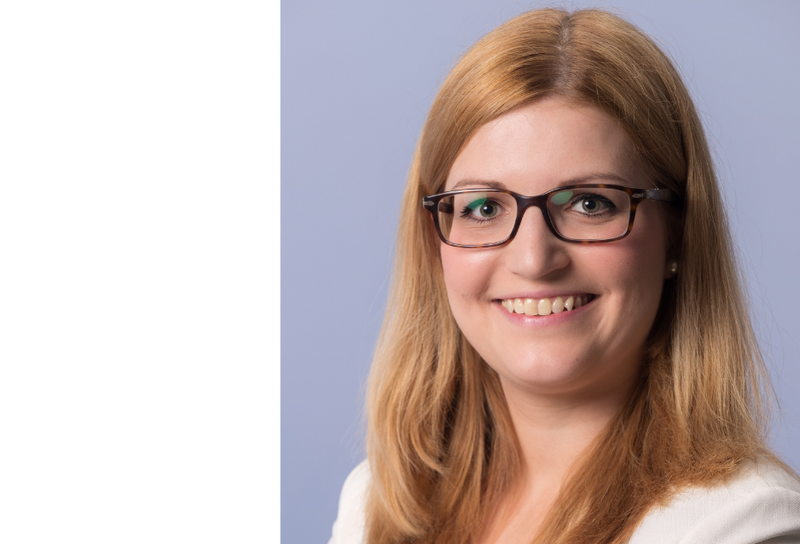 Die Person hat helle lange Haare und eine Brille. Sie trägt ein weißes Hemd.