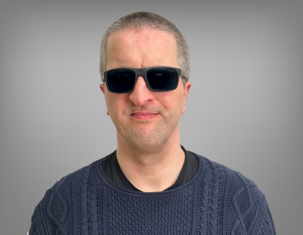 Portrait von Fredrik Fischer. Fredrik hat kurze graue Haare, trägt eine Sonnenbrille. Er trägt einen dunkelblauen Pullover.