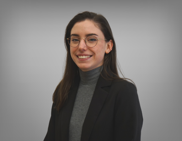 Portrait of Antonia Cichocki. She wears glasses and has dark brown hair. She is wearing a grey T-shirt with a black blazer.