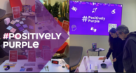 Fotocollage eines Infostands mit Materialien und dem groß eingeblendeten Text „#POSITIVELY PURPLE“; im Hintergrund ein Bildschirm mit „# Positively Purple“, Piktogrammen und einem QR-Code, davor zwei Personen an einem Tisch.