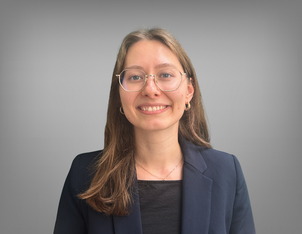 Portrait von Verena Aistleitner. Sie hat lange, braune und glatte Haare. Sie trägt eine Brille mit einem Metall Rahmen und Ohrringe. Sie trägt ein schwarzes T-Shirt mit einem dunklen Blazer.