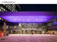 Frontansicht der Bahnhofshalle am Wiener Hauptbahnhof in violett beleuchtet.