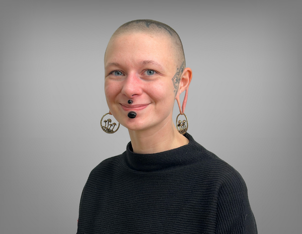 Portrait von Annika Candy. Sie hat eine Glatze, Tattoos und Piercings. Sie trägt einen schwarzen Pullover.
