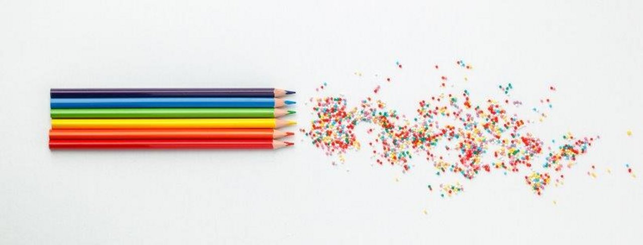 Verschieden färbige Buntstifte in einer Reihe. Daneben die Reste vom Anspitzen der Stifte. 