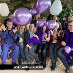 Screenshot eines Videos, in dem ca. 10 lila gekleidete Mitarbeitende von Bayer Austria lila Luftballons in die Höhe werfen