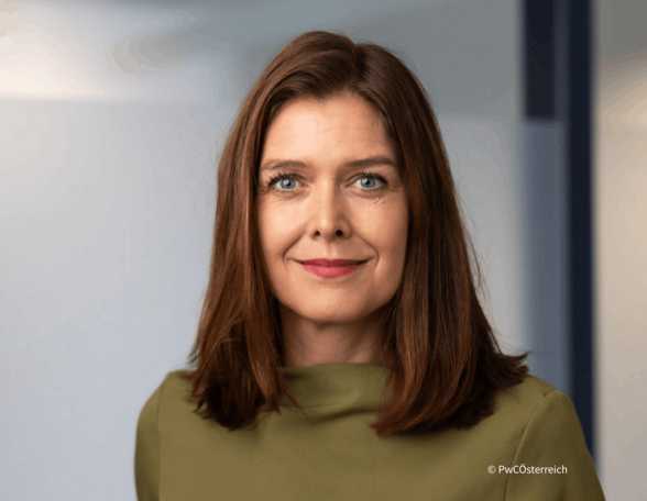 Person mit schulterlangen braunen Haaren und olivgrünem Top lächelt in die Kamera.