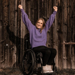 Kira Grünberg mit lila Oberteil streckt ihre Arme in die Höhe und sitzt in einem Rollstuhl