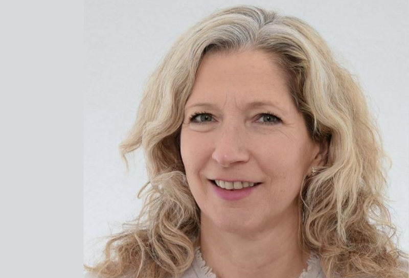 Person hat lange helle Haare. Sie trägt Ohrringe und eine beiges Oberteil. 