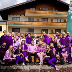 Ein großes Team, alle mit lila Kleidung vor einem ländlichen Gebäude.