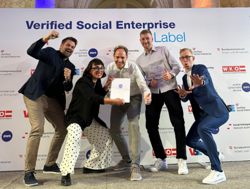 Wolfgang Kowatsch, Fides Raffel, Michael Aumann, Sebastian Stoll und Michael Zakall posieren freudig mit dem Label/Zertifikat "Verified Social Enterprise" vor einer Logowand. Logos WKO, SENA, aws, Bundesministerium für Arbeit und Wirtschaft